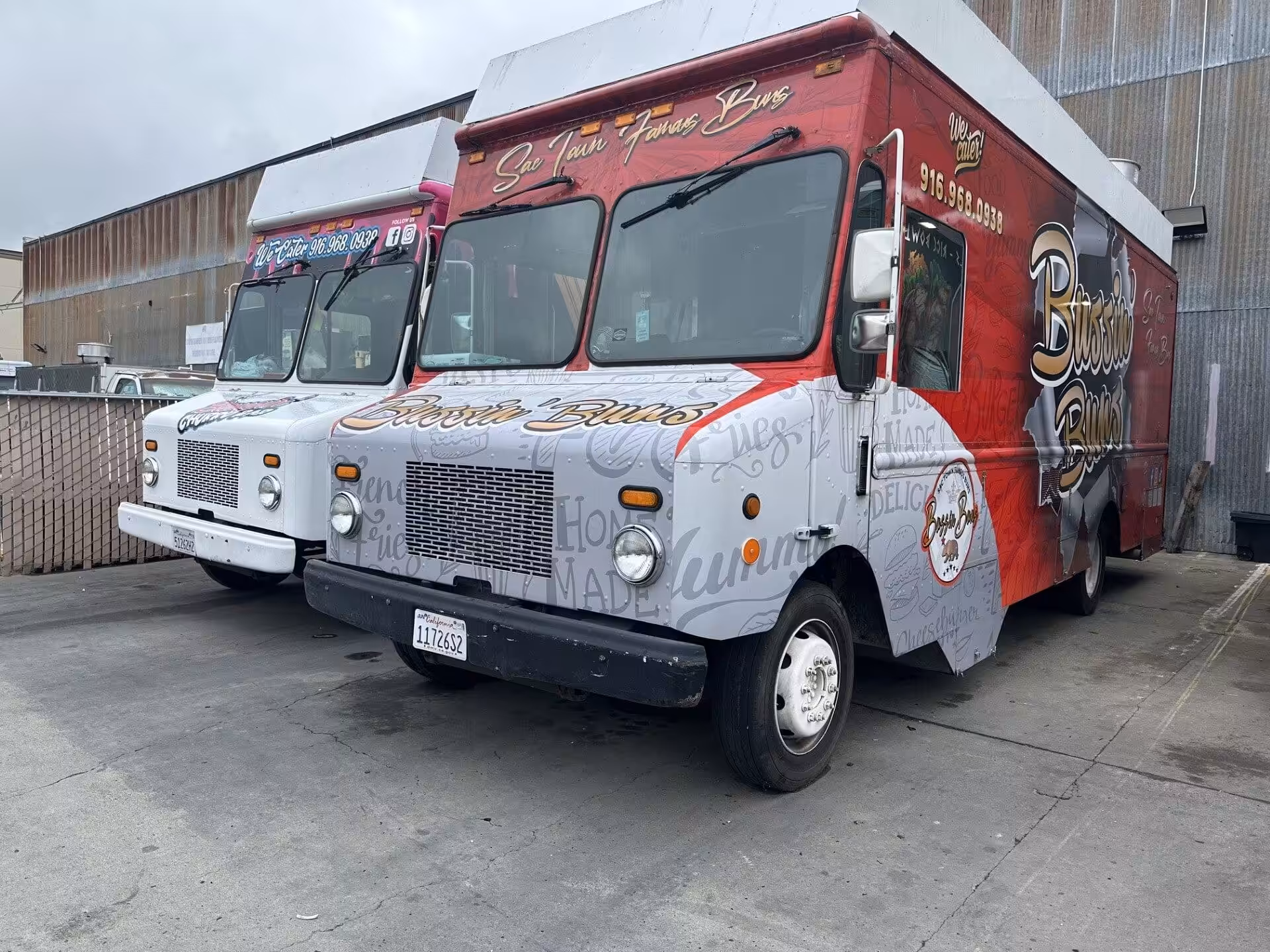 Two vibrant food trucks parked side by side, featuring bold graphics and text advertising gourmet burgers against an industrial backdrop.